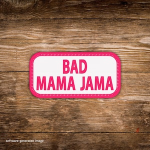 May include: A rectangular patch with the words "BAD MAMA JAMA" in bright pink letters on a white background. The patch has a pink border and is set against a wooden background.