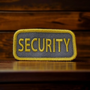 May include: A yellow and gray embroidered patch with the word "SECURITY" in yellow lettering.