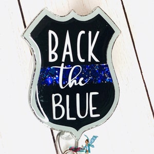 Könnte beinhalten: Ein schwarzer und silberner, badgeförmiger, einziehbarer Ausweishalter mit einem blauen Glitzerstreifen und dem Text "Back the Blue".