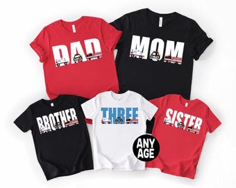 May include: A collection of five short-sleeved t-shirts in red, black, and white. The shirts feature the words DAD, MOM, BROTHER, THREE, and SISTER in large white or blue letters, decorated with small ambulance, police car, and fire engine graphics.