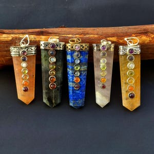 Könnte beinhalten: Fünf Edelsteinanhänger mit silberfarbenen Metallkappen und Schlaufen. Jeder Anhänger hat einen andersfarbigen Stein, darunter Orange, Grün, Blau, Rosa und Gelb. Kleine, farbige Steine sind in der Mitte jedes Anhängers angeordnet.