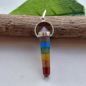 Könnte beinhalten: Ein mehrfarbiger Chakra-Anhänger mit silberfarbener Öse. Der Anhänger hat Bänder in Rot, Orange, Gelb, Grün, Blau und Lila. Der Anhänger ist etwa 5 cm lang.