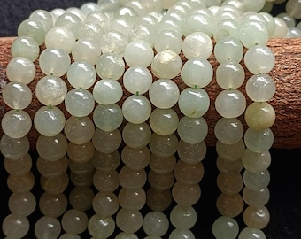 Op de afbeelding: Close-up van strengen lichtgroene jade kralen. De kralen zijn rond en hebben een glad, gepolijst oppervlak. De jade kralen zijn geregen aan een groene draad. De kralen zijn een mix van lichte en medium groene tinten.