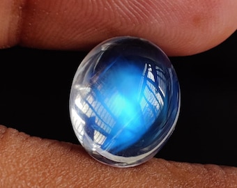 May include: A round, oval-shaped, iridescent gemstone with a blue and white color. The gemstone is smooth and polished.