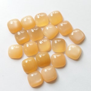 May include: A collection of 17 smooth, light orange, square-shaped gemstone cabochons.