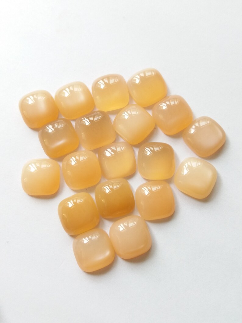 May include: A collection of 17 smooth, light orange, square-shaped gemstone cabochons.