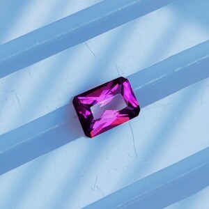May include: A vibrant purple gemstone with a rectangular shape, cut with facets, and a glossy finish.