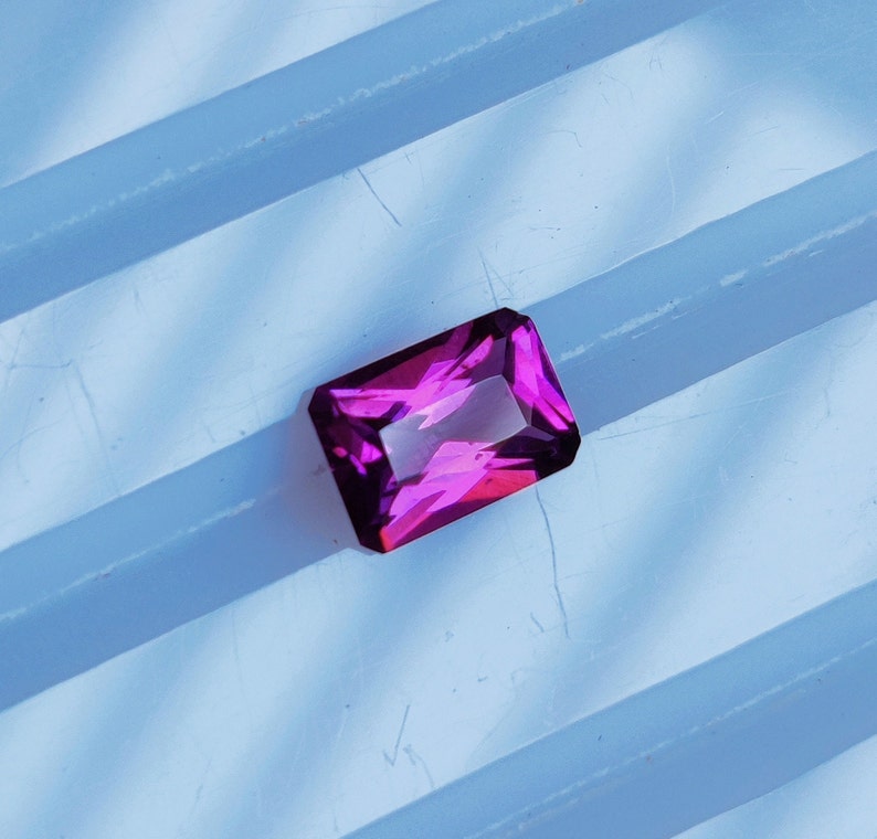 May include: A vibrant purple gemstone with a rectangular shape, cut with facets, and a glossy finish.
