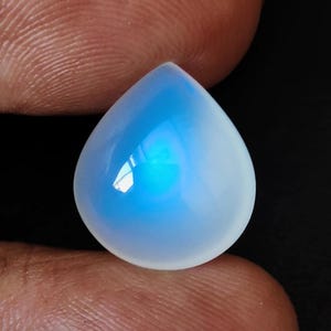 Puede incluir: Un cabujón de piedra lunar en forma de lágrima, iridiscente, de color azul y blanco.