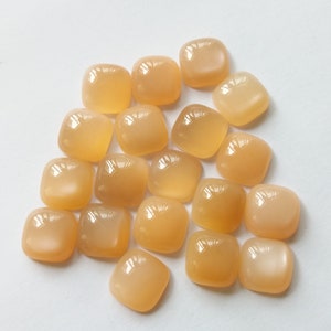 May include: A collection of 18 smooth, square-shaped, light orange gemstones with a pearlescent sheen.