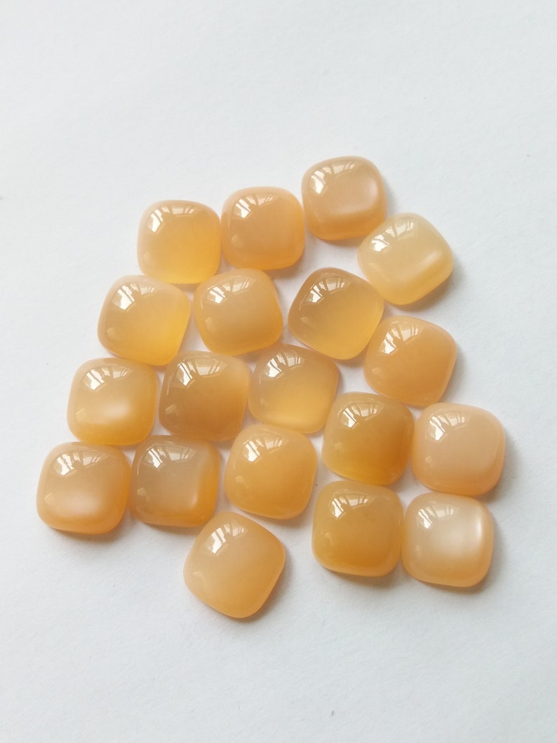 May include: A collection of 18 smooth, square-shaped, light orange gemstones with a pearlescent sheen.