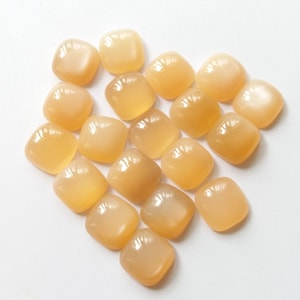 May include: A collection of 18 smooth, light orange, square-shaped gemstones. The stones are arranged in a heart shape on a white background.