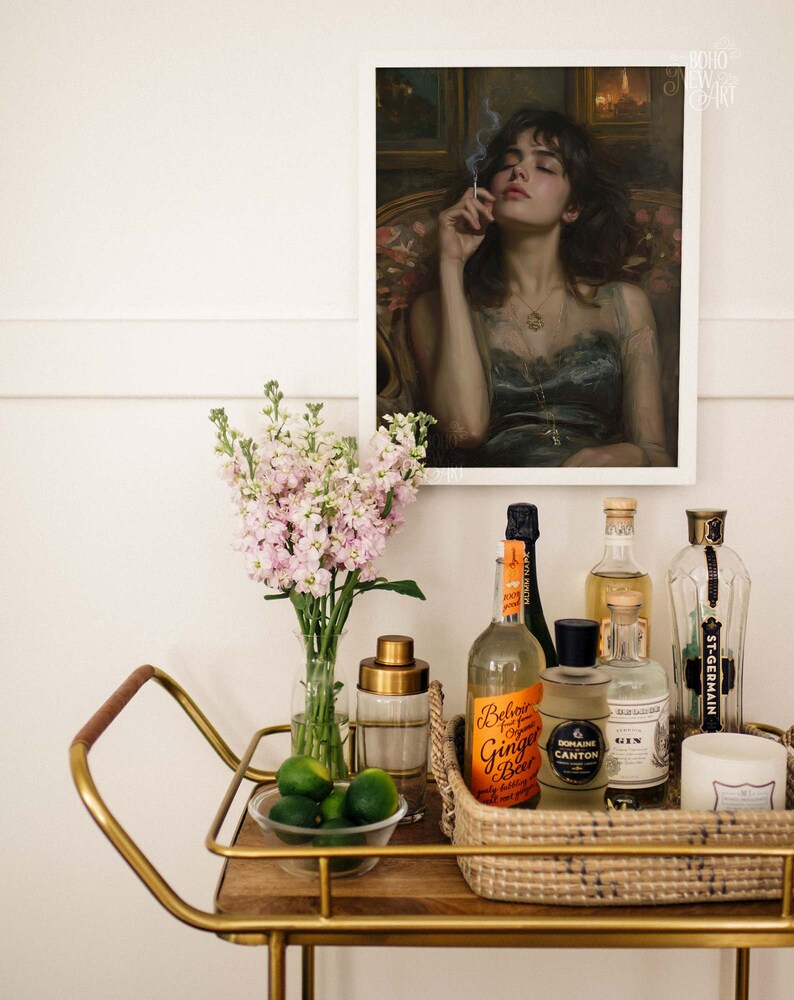 May include: A gold bar cart with a wooden top and a wicker basket filled with various bottles and a candle. The bottles include a clear bottle of ginger beer, a clear bottle of gin, a dark bottle of Domaine Canton, and a clear bottle of St-Germain. There are also limes in a glass bowl on the cart.