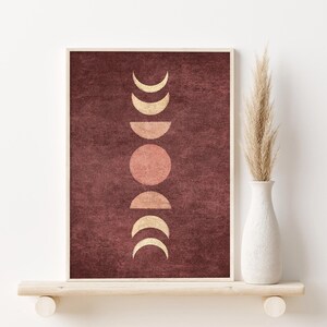 May include: A framed print with a maroon background and a vertical arrangement of gold and pink moons in different phases.