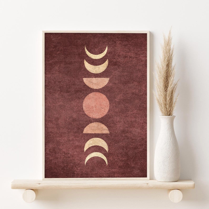 May include: A framed print with a maroon background and a vertical arrangement of gold and pink moons in different phases.