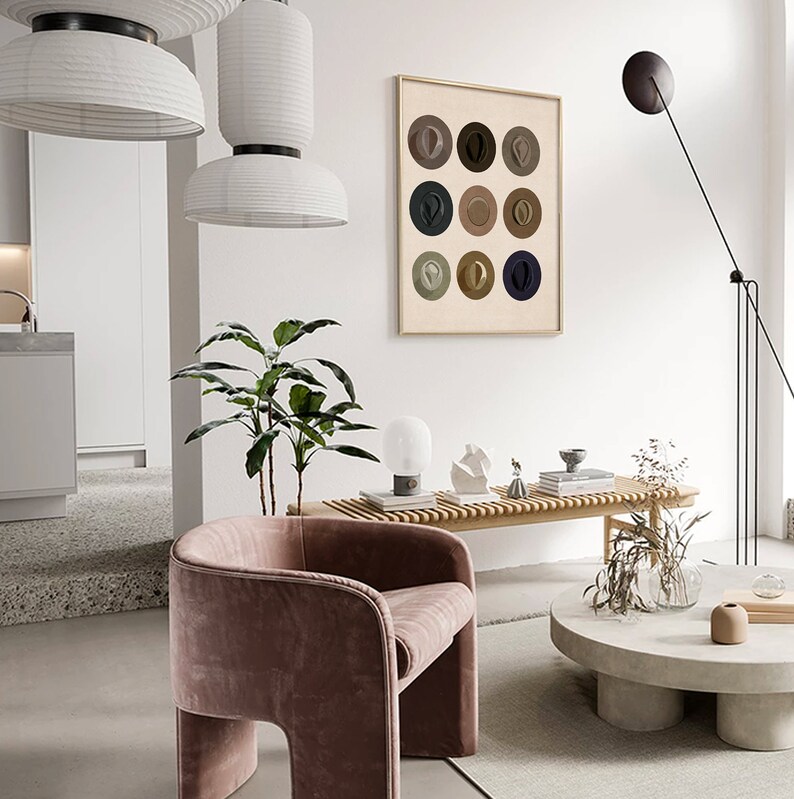 May include: A framed print of a minimalist art piece featuring nine circles with different colored hats inside each circle. The print is hanging on a white wall in a modern living room with a pink velvet armchair, a wooden bench, and a concrete coffee table.