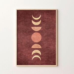 May include: A digital art print featuring a stylized moon phases design in gold and peach on a burgundy background. The print is framed in a light wood frame.