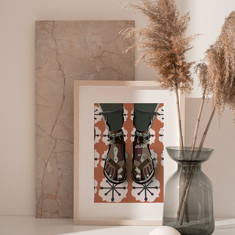 May include: A framed art print featuring a stylized illustration of feet wearing brown sandals with decorative anklets. The sandals have a geometric design. The background shows a patterned orange and white tile floor.