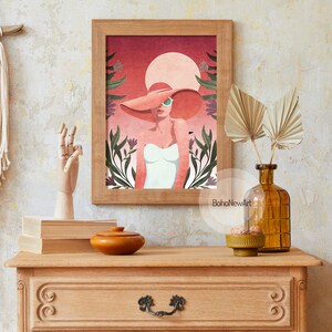 May include: A framed illustration of a woman wearing a large pink hat and sunglasses, standing in front of a pink and orange sunset with green foliage. The text "BohoNewArt" is at the bottom of the image.