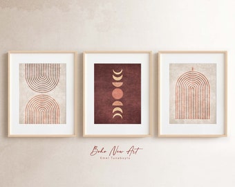 May include: Three framed art prints with a boho theme. The prints feature abstract designs in shades of red and beige. One print has a series of curved lines, another has a moon phase design, and the third has a curved arch design. The frames are light wood.