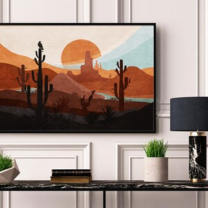 May include: A framed print of a desert landscape with a sunset, mountains, and cacti. The print is in a black frame and is hanging on a white wall.
