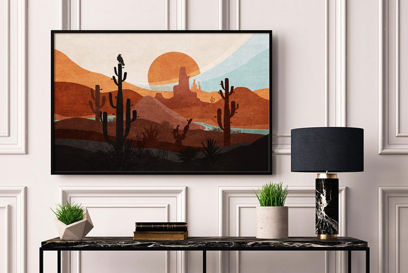 May include: A framed print of a desert landscape with a sunset, mountains, and cacti. The print is in a black frame and is hanging on a white wall.