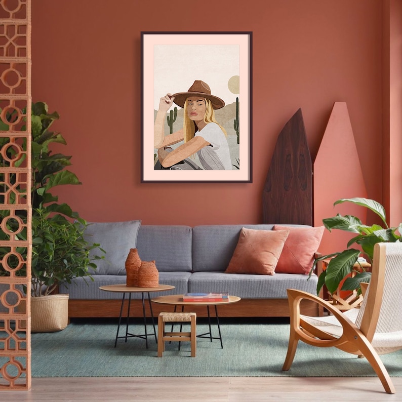 Puede incluir: Una ilustraci&oacute;n enmarcada de una mujer con un sombrero marr&oacute;n y una camisa blanca, sentada en un paisaje des&eacute;rtico con cactus.