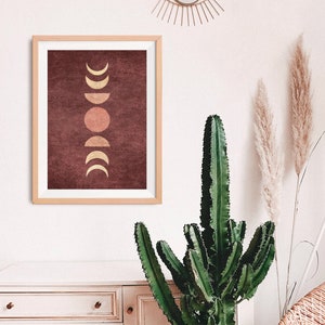 May include: A framed print with a maroon background and a gold moon phases design. The moon phases are in a vertical line, with a full moon in the center.