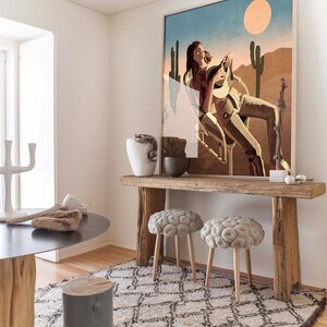 Peut inclure: Une console en bois rustique avec deux poufs en tricot gris. La table a une finition vieillie et est d&eacute;cor&eacute;e d'une grande estampe encadr&eacute;e d'une femme assise dans un paysage d&eacute;sertique avec des cactus.