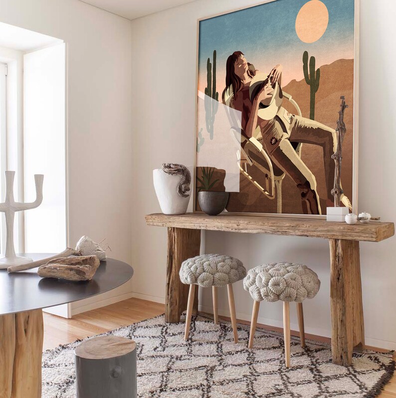 Peut inclure: Une console en bois rustique avec deux poufs en tricot gris. La table a une finition vieillie et est d&eacute;cor&eacute;e d'une grande estampe encadr&eacute;e d'une femme assise dans un paysage d&eacute;sertique avec des cactus.