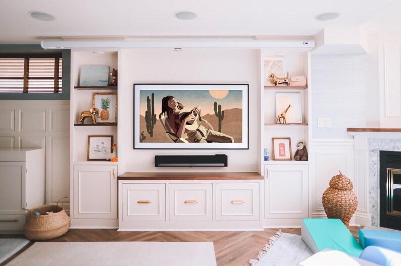 May include: A modern living room entertainment center with a large framed artwork depicting a desert scene. The room features built-in cabinets, shelves with decorative items, and a fireplace. A soundbar is mounted below the TV.
