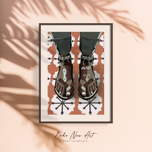 May include: Framed art print featuring a stylized illustration of feet wearing brown sandals with decorative anklets. The sandals have turquoise accents and are set against a patterned background. The artwork is signed "Boho New Art" by Emel Tunaboylu.