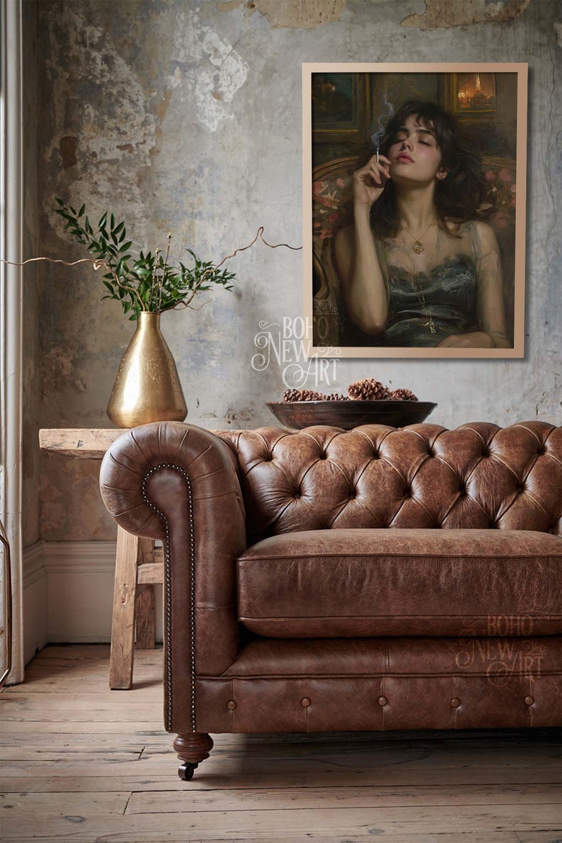May include: A brown leather chesterfield sofa with button tufting sits in front of a wall with a framed painting of a woman in a blue dress holding a cigarette. The painting is set against a dark background with a small framed picture above it.