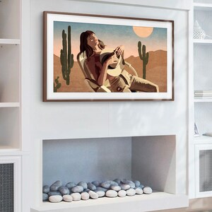 May include: A framed art print depicts a person relaxing in a chair in a desert landscape. The artwork features a warm color palette with a sun, cacti, and a person wearing a hat. The frame is a dark brown color.