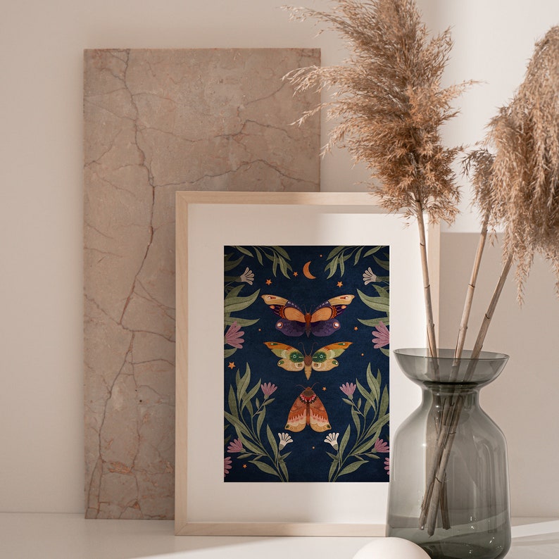 May include: A framed print with a dark blue background featuring three colorful butterflies and a crescent moon surrounded by green leaves and white flowers.