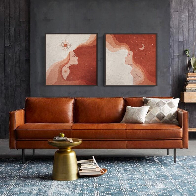 Puede incluir: Dos impresiones enmarcadas cuadradas de arte abstracto con un rostro de mujer y cabello suelto. Las impresiones est&aacute;n colgadas en una pared gris oscuro sobre un sof&aacute; de cuero marr&oacute;n con dos almohadas.
