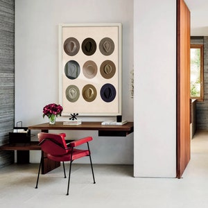 May include: A red chair with black metal legs sits in front of a desk with a framed print of nine abstract circles in shades of brown and gray. The print is titled "Paul de Saint"