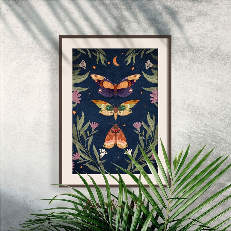 May include: A framed print with a dark blue background featuring three colorful moths with intricate patterns and a crescent moon. The moths are surrounded by green leaves and pink flowers.