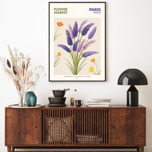 May include: A vintage botanical illustration of purple flowers with yellow flowers in the background. The illustration is framed and hanging on a white wall above a wooden cabinet. The text "FLOWER MARKET" and "PARIS FRANCE" is printed at the top of the illustration.