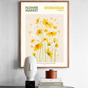 May include: A framed poster with a watercolor illustration of yellow flowers on a beige background. The poster has the text "FLOWER MARKET" and "STOKHOLM SWEDEN" at the top. The text "FLOWERS OF CITIES - CURATED ART COLLECTION" is at the bottom.