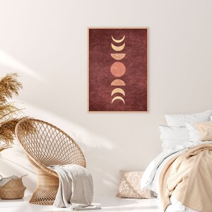 May include: A framed print with a minimalist design featuring a series of gold crescent moons and a single red circle on a burgundy background.