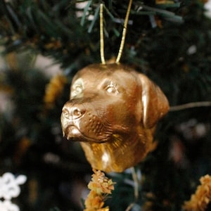 May include: A gold-colored dog ornament hanging on a Christmas tree. The ornament is detailed and realistic, with a textured surface.