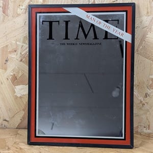 Könnte beinhalten: Gerahmtes TIME-Magazin-Cover mit schwarzem Hintergrund und dem Titel "TIME" in großen, fetten Buchstaben. Der Rahmen ist schwarz mit einem roten Rand. Ein weißes Banner oben zeigt "MAN OF THE YEAR". Der Text "THE WEEKLY NEWSMAGAZINE" steht unten.