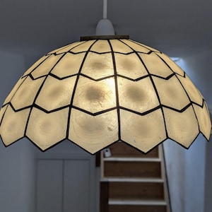 May include: A dome-shaped pendant light fixture featuring a series of translucent, off-white, shell-like panels arranged in a repeating chevron pattern. The individual panels are outlined with dark, thin metal lines, creating a geometric grid.
