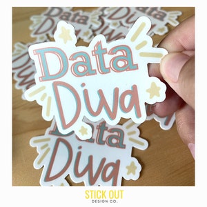 Könnte beinhalten: Ein weißer Aufkleber mit dem Text "Data Diva" in rosa und blauen Buchstaben mit gelben Sternen und Lichtstrahlen um den Text. Der Aufkleber wird von einer Hand gehalten und im Hintergrund befinden sich weitere Aufkleber.