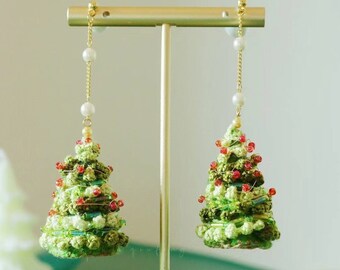 May include: A pair of green and red Christmas tree earrings with white pearl accents hanging from a gold stand.
