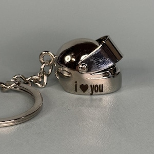 May include: Silver keychain with a helmet charm. The helmet has a visor and the words "I love you" engraved on the side.
