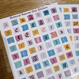 Puede incluir: Hojas de pegatinas con letras de estilo medieval en varios colores. Las pegatinas están dispuestas en un patrón de cuadrícula, con cada letra sobre un fondo de color diferente. El texto "Medieval Ransom Note Stickers" está en la parte superior.