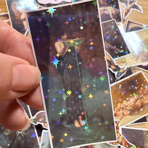 Puede incluir: Una pegatina rectangular con una pintura cl&aacute;sica oscura de una figura sosteniendo un cuenco, superpuesta con un patr&oacute;n de estrellas hologr&aacute;ficas. La pegatina tiene un borde blanco y muestra a una persona con una prenda larga y oscura.