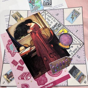 Pu&ograve; includere: Una collezione di articoli a tema tarocchi che include un tabellone di gioco stampato con sezioni numerate, una carta rettangolare con una donna in abito rosso che tiene una sfera di cristallo, un adesivo olografico e un piccolo adesivo a forma di freccia.